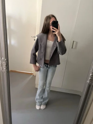 Grå kappa från Gina Tricot - Säljer en stilren grå kappa från Gina Tricot med dubbelknäppning och bred krage. Jackan har en croppad passform och raka ärmar, perfekt för dig som vill ha en trendig och enkel look. Materialet känns mjukt och passar till många outfits.
