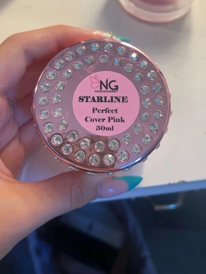 NG Starline Cover Pink nagelgel 30ml - Redan Nerprutad !!Nagelgel från NG Starline i färgen Cover Pink. Burken rymmer 30 ml och har ett lyxigt lock dekorerat med glittrande stenar. Gelen har en mjuk rosa ton som ger en naturlig och fräsch look till naglarna. Perfekt för att bygga eller förstärka naglar.