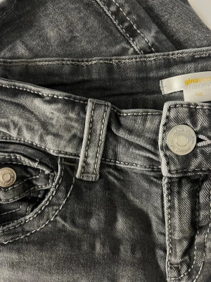 Gina Tricot jeans - Snygga grå jeans från Gina Tricot i bootcut-modell med coola detaljer på bakfickorna och silvriga knappar. Jeansen har klassisk femficksdesign och är tillverkade i denim med lätt tvättad look. Perfekta för en trendig vardagsstil.