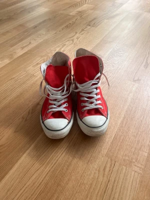 Röda Converse All Star high tops - Klassiska röda Converse All Star high tops med vit tå och sula, vita skosnören och den ikoniska loggan på sidan. Skorna är i canvasmaterial och har svart rand längs sulan. Perfekta för en cool och avslappnad stil.