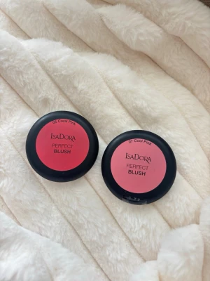 IsaDora Perfect Blush duo rosa - Två IsaDora Perfect Blush i nyanserna 05 Coral Pink och 07 Cool Pink. Båda har rund form och kommer i svarta plastdosor med rosa etikett. Perfekt för att ge kinderna en fräsch rosa ton. Oöppnade och helt nya.