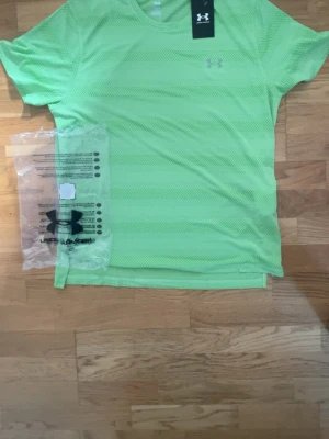 Grön tränings-tshirt Under Armour - Snygg grön tränings-tshirt från Under Armour med rund hals och korta ärmar. Tillverkad i ett lätt och ventilerande meshmaterial som passar perfekt för intensiva träningspass. Diskret logga på bröstet och sportig passform.
