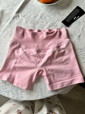 Aura seamless scrunch shorts Relode  - Säljer ett par ljusrosa träningstights shorts från Relode i storlek XS. De har hög midja med bred ribbad linning för extra stöd och är tillverkade i ett mjukt och stretchigt material som passar perfekt till gymmet eller andra aktiviteter.