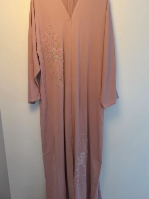 Lång ljusrosa abaya med broderi - Ljusrosa abaya med broderi. Helt nytt skick. Sjal medföljer