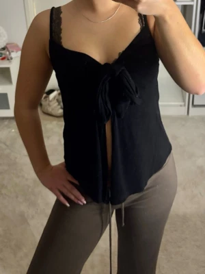 Svart topp med knyt  - Snygg svart topp med knyt framtill. Modellen har en djup urringning och tunna axelband. Tyget är mjukt och stretchigt, perfekt för en trendig look. Skriv vid frågor eller funderingar💕