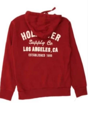 Röd hoodie från Hollister - Röd hoodie från Hollister med tryck i vitt på ryggen där det står 'Hollister Supply Co. Los Angeles, CA Established 1999'. Klassisk huva och ribbade muddar. Perfekt för en avslappnad och cool stil. Pris går att diskutera!!