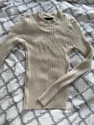 Beige ribbstickad tröja från PIECES - Snygg beige ribbstickad tröja från PIECES med lång ärm och högre rundad hals. Tröjan har en tight passform och är gjord i mjukt, stretchigt material som sitter skönt på kroppen
