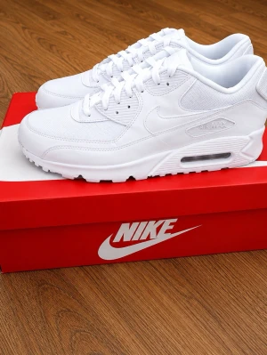 Nike Air Max 90 helvita - Nike Air Max 90 sneakers i helvitt med klassisk sula och synlig Air-enhet. Ovandelen är i mesh och läder för både stil och komfort. Ikonisk swoosh på sidan och detaljerade sömmar ger en clean och modern look. Perfekta för dig som gillar streetwear och sportig stil.