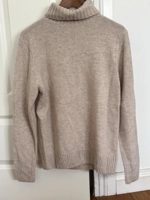 Beige polotröja från Bläck - Mysig beige stickad polotröja från Bläck i storlek S. Tröjan har ribbstickade muddar vid ärmslut och nederkant samt en hög, vikt polokrage. Perfekt för kalla dagar och enkel att matcha med olika outfits.