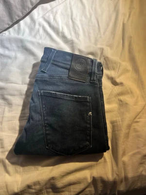 Replay anbass hyperflex  - Snygga mörkblå slim fit jeans med klassisk femficksdesign och subtila slitningar. Jeansen har en patch bak i midjan och raka ben. Perfekta för dig som gillar en stilren och enkel look till vardags. Strl 27/30