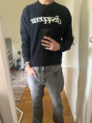 Svart sweatshirt med vit text - Svart sweatshirt med vit tryckt text över bröstet. Tröjan har rund halsringning, långa ärmar och ribbade muddar vid ärmslut och nederkant. Perfekt för en avslappnad och stilren look. Storlek XS, sitter mer som S