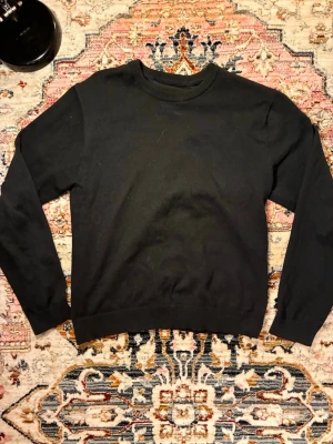 Svart basic sweatshirt - En enkel svart sweatshirt med rund halsringning och långa ärmar. Tröjan har ribbade muddar vid ärmslut och nederkant. Perfekt för en avslappnad och stilren look. Tröjan har ett litet hål i nacken men inget som påverkar användningen 