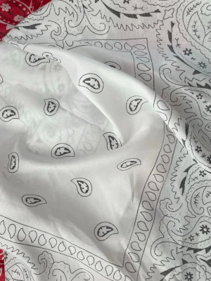Bandana - Säljer en vit sjal med klassiskt paisleymönster i svart. Sjalen är fyrkantig och har tunnt, mjukt tyg som känns skönt mot huden. Perfekt att knyta runt halsen eller i håret för en cool och stilren look.