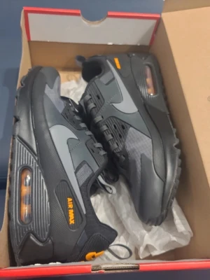 Nike Air Max 90 Drift stl. 41  - Snygga Nike Air Max sneakers i svart och mörkgrått med orange detaljer. Det finns en liten sprick på skorna som ni ser på bilden men den syns knappt när man har skorna på sig och det påverkar 100% inget. Skorna är köpte direkt från JD och kommer med box och allt annat! PRISET ÄR INTE HUGGET I STEN!! 🤝🤝🔥🔥 