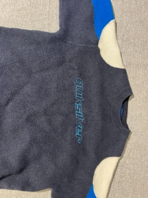 Blå fleece tröja från Quiksilver - Blå fleece tröja från Quiksilver med broderad logga på bröstet. Tröjan har rund halsringning och kontrastpaneler i vitt och blått på ärmarna. Pris går att diskuteras!