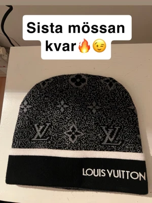 Svart mössa - Snygg svart mössa med klassiskt monogrammönster i grått och vit kant. Märkets logga är broderad framtill på uppviket. Perfekt accessoar för dig som vill ha en exklusiv och trendig look. 
