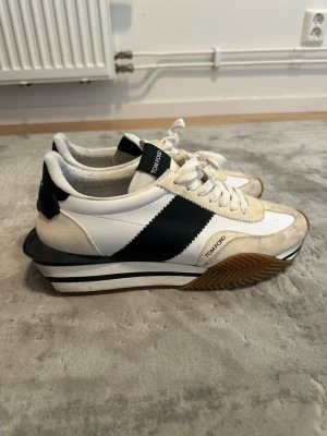 Tom Ford vita sneakers med platåsula - ORGINAL PRIS≈950€, finns lite smuts på dem som går att tvätta bort enkelt!!!Säljer ett par vita sneakers från Tom Ford med beige mockadetaljer och svart diagonal stripe på sidan. Skorna har en unik platåsula i vitt, svart och brunt gummi samt vita snören. Klassisk retrostil med modern twist och tydlig Tom Ford-logga på plösen.