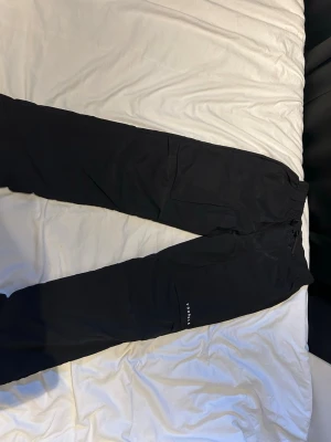 Youngla cargo pants - Säljer ett par svarta mjukisbyxor med resår i midjan och ett diskret tryck på benet. Byxorna har avslappnad passform och är perfekta för chill dagar. Materialet känns mjukt och bekvämt, och de har en enkel, stilren look.