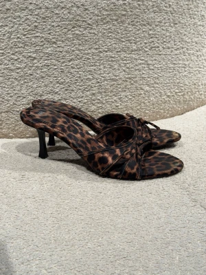 Leopardmönstrade pumps från Zara - Säljer ett par snygga klackskor från Zara med leopardmönster i bruna och svarta toner. Skorna har öppen tå, smal klack och rosett.