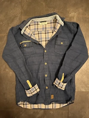 Blå overshirt från Anerkjendt - Snygg blå overshirt från Anerkjendt med rutigt innerfoder i blått och beige. Skjortan har långa ärmar, två bröstfickor med knappar och kontrastdetaljer i gult vid ärmslut och ficka. Perfekt lager-på-lager-plagg för en avslappnad stil.