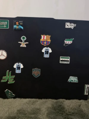 Mixade pins och märken fotboll & flaggor. - Säljer ett set med olika pins och märken med motiv som fotbollströjor, flaggor, logotyper och symboler från bland annat Saudiarabien, Barcelona och Mercedes. Färgerna är främst grönt, vitt, blått och gult. Kommer med en dubbelsidig tejp som går att häfta på en mobil, dator, ipad osv.tejpen är gjord så att den Förstör inte platsen den ligger på.  1st 50:- kronor      2st 80:-  kronor    3st 100:-  kronor