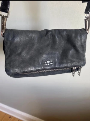 Svart Zadig & Voltaire väska - Svart Zadig väska med avtagbar axelrem så den kan bäras som clutch. Väskan har en vikbar design. Ringarna som håller i axelremmen har blivit lite slitna i silverfärgen, se bild. 