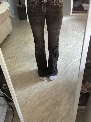 Bootcut jeans med kontrastsömmar - Snygga bootcut jeans i mörkgrå tvätt med vita kontrastsömmar och klassiska fem fickor. Jeansen har låg midja och utsvängda ben, vilket ger en retro vibe. Perfekta för dig som vill ha en avslappnad men trendig look.