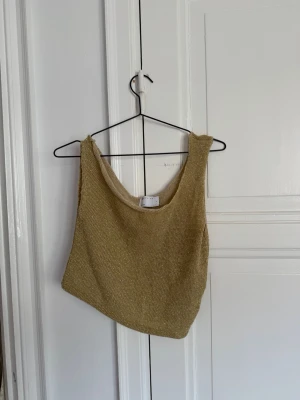 ASOS - Guldig stickad croppad linnetopp - Snygg guldig linnetopp i stickat material med croppad passform. Toppen är ärmlös och har en enkel, stilren design som passar perfekt till sommarens outfits.
