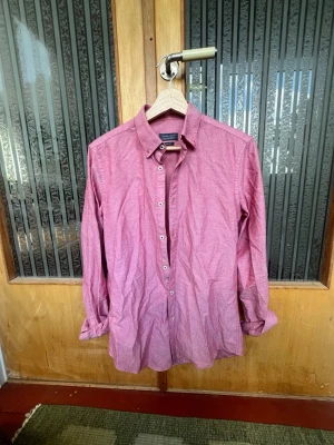 Rosa skjorta från Zara Man slim fit - Säljer en stilren rosa skjorta från Zara Man i slim fit-modell. Skjortan har klassisk krage, långa ärmar och vita knappar framtill. Perfekt för dig som gillar en enkel men snygg look. Materialet är mjukt och skönt bomullstyg.