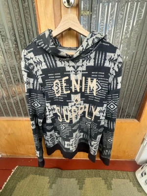 Mönstrad hoodie från Denim & Supply - Säljer en svart och grå hoodie från Denim & Supply Ralph Lauren med coolt etnomönster och stor text på bröstet. Hoodien har huva och ribbade muddar vid ärmar och nederkant. Perfekt för dig som vill sticka ut med en unik stil.