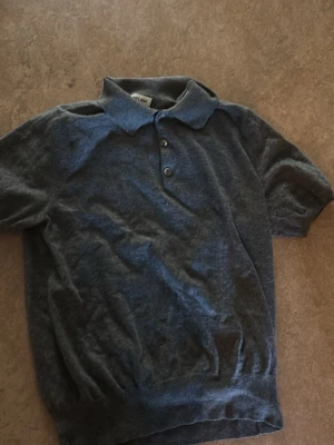 Grå pikétröja från Soft Goat - Mjuk och stilren grå pikétröja från Soft Goat i exklusiv kashmir. Tröjan har korta ärmar, klassisk krage och tre knappar framtill. Perfekt för dig som gillar en avslappnad men ändå snygg look. Storleken är XXL. Själv har jag S/M och den passar mig.