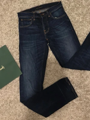 Grim Tim Nudie - Säljer ett par mörkblå jeans från Nudie Jeans           Modell: Grim Tim                                                                Storlek: 29/32                                                                    Skick: 9/10 Inga defekter.                                                21cm lårmått. 103cm längd. 16cm benöppning.