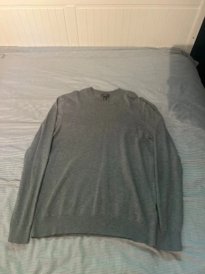 Grå slim fit tröja från H&M - Snygg grå tröja från H&M i slim fit-modell. Tröjan har rund halsringning, långa ärmar och ribbade muddar vid ärmslut och nederkant. Perfekt för en stilren och enkel look.
