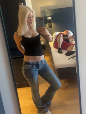 Tru religion jeans men glitter på fickorna  - Säljer ett par blå bootcut jeans med låg midja och klassiska fickor bak. Jeansen har en avslappnad passform och lätt slitningar för en cool look. Perfekta för dig som gillar en retro vibe och vill ha ett par jeans som sticker ut.