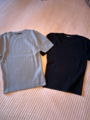 Två stickade t-shirts i blått och svart storlek xs - Säljer två stickade t-shirts i klassisk modell, en i ljusblå och en i svart. Båda har rund halsringning och korta ärmar. Perfekta att matcha till jeans eller kostymbyxor för en enkel och clean look. 70% viscos 30% polyamid.