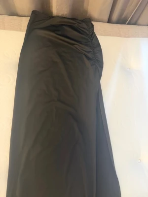 Svart långkjol med slits från SHEIN - Stilren svart långkjol från SHEIN i storlek XS Petite. Kjolen har en snygg slits på sidan och lätt rynkade detaljer upptill för en trendig look. Tillverkad i mjukt och följsamt material som passar perfekt till olika outfits.