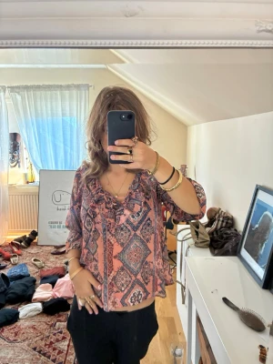 Mönstrad boho-blus i rosa och blått - Säljer en luftig boho-inspirerad blus med rosa och blått mönster. Blusen har trekvartsärm och snörning med volangdetalj vid halsen. Perfekt för dig som gillar avslappnad och trendig stil. Materialet känns lätt och flowy.