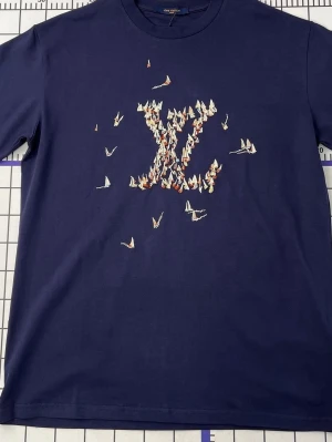 Mörkblå t-shirt med broderad - Snygg mörkblå t-shirt med broderad  -logga framtill, där loggan är formad av små färgglada segelbåtar. Klassisk rund hals och korta ärmar. Perfekt för dig som gillar exklusiva detaljer och stilren design.