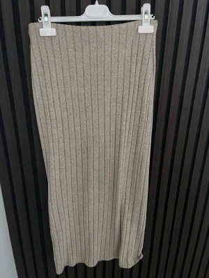 Beige ribbad långkjol - Stilren beige långkjol i ribbad design. Kjolen har en rak passform och är tillverkad i ett mjukt stickat material som ger en skön känsla. Perfekt att matcha med en enkel topp eller stickad tröja för en avslappnad look.
