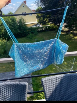 Blå glitter topp - Från Gina tricot.  Säljer en blå bandeau topp med tunna axelband och glittriga paljetter över hela tyget. Perfekt för dig som vill sticka ut och glänsa lite extra. Toppen har en croppad passform och är superfin till både jeans och kjol.