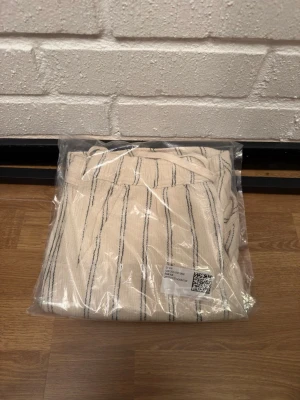 Beige linnebyxor med svarta ränder - Säljer ett par beige linnebyxor med tunna svarta vertikala ränder. Byxorna har resår i midjan och är tillverkade i ett luftigt linnematerial, perfekta för en avslappnad och trendig look.