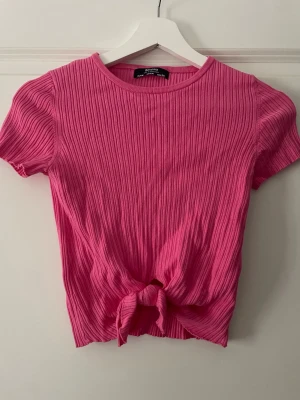 Ribbad rosa topp  - Säljer en croppad ribbad rosa topp från Bershka med korta ärmar och knut framtill. Endast använd 1 gång.