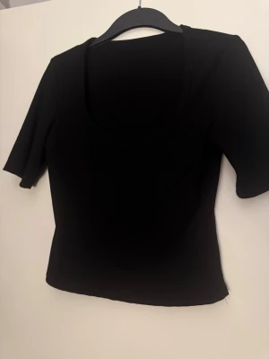 Svart topp med trekvartsärm strl M - En stilren svart ribbad topp med trekvarts ärmar och rundad urringning. Perfekt att matcha med jeans eller kjol för en clean look. 