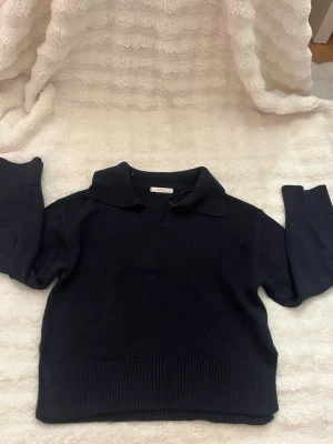 Svart stickad tröja med krage - Mysig svart stickad tröja med bred krage och v-ringning. Tröjan har långa ärmar och ribbstickade muddar samt nederkant. Perfekt för lager-på-lager och enkel att matcha med jeans eller kjol.