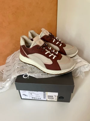 Beige och vinröda sneakers från Ecco, stl 36 nya , äkta skinn  - Snygga sneakers från Ecco i beige och vinrött med vita detaljer. Skorna har en sportig design med lågt skaft, vita snören och en bekväm sula. Materialmix av mocka och textil ger en modern look. Perfekta för dig som gillar stilrena och trendiga sneakers. Stl 36, äkta skinn