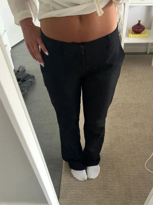 Svarta raka kostymbyxor - Snygga svarta kostymbyxor med rak passform och medelhög midja. Byxorna har diskret dragkedja framtill och är tillverkade i ett mjukt, vävt tyg som ger en clean look. Perfekta för dig som gillar stilrena och klassiska plagg. Lite noppriga i knäveck men inget som syns!