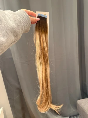 Långt löshår med balayage-effekt - Snyggt löshår med tejpfästen i en naturlig balayage med mörkbrun botten och ljusare blonda längder. Håret är rakt och har en mjuk glans. Perfekt för dig som vill ha extra längd och volym. Material: äkta hår. Säljer då jag köpte för mycket, 