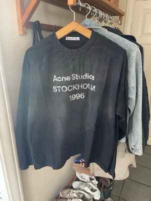 Svart långärmad Acne Studios - Säljer en svart långärmad topp från Acne Studios med tryck i vitt framtill där det står 'Acne Studios STOCKHOLM 1996'. Klassisk rund halsringning och avslappnad passform. Perfekt för dig som gillar stilrena och trendiga plagg.