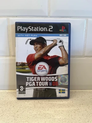 Tiger Woods PGA Tour 08 PS2 spel - Golfspel till PlayStation 2 med Tiger Woods PGA Tour 08. Omslaget är blått med bild på Tiger Woods i röd tröja och svart keps. Spelet har svensk flagga på framsidan och är rekommenderat från 3 år. Perfekt för dig som gillar sportspel och golf.