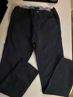 Mörkblå chinos med rak passform - Snygga mörkblå chinos med klassisk rak passform och bälteshällor. Tillverkade i ett mjukt bomullstyg som ger en skön känsla. Fickor på sidorna och baktill. Perfekta för en clean och stilren look.